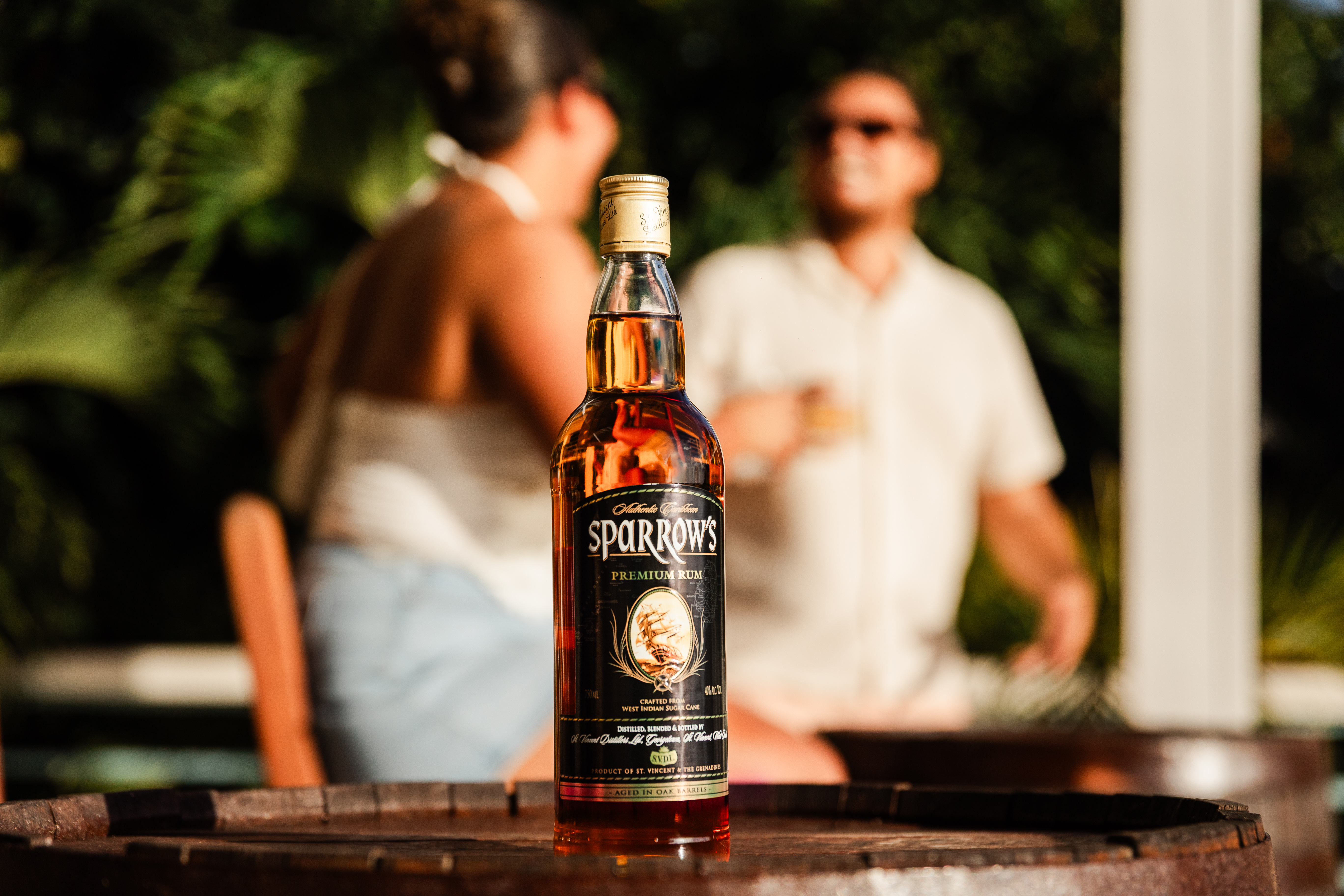Sparrow's Premium Old Rum bottle standing on a rustic wooden table with a blurred distillery background