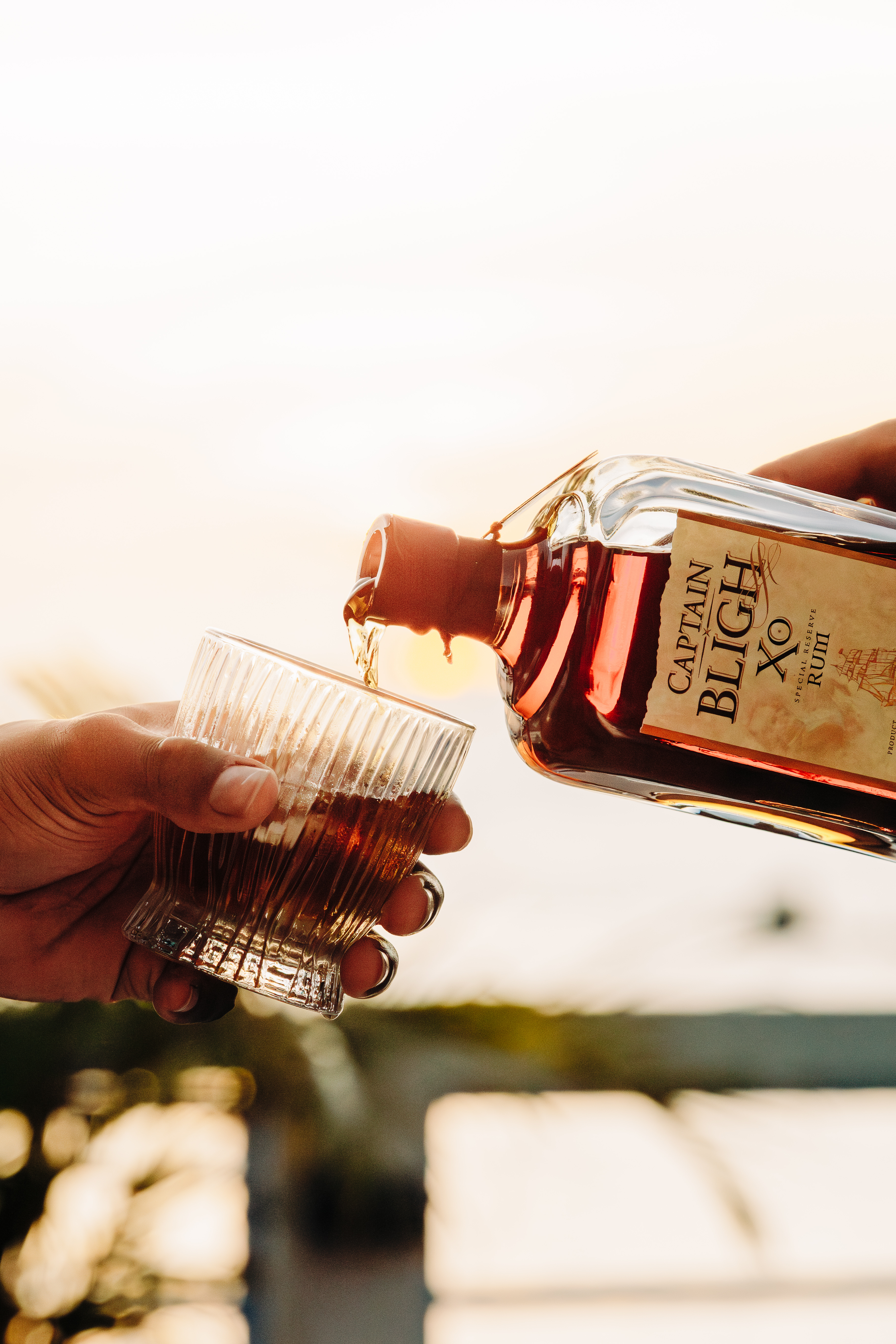 Sunset Captain Bligh XO rum bottle with clear glass and aged barrels in background
